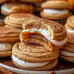 Golden brown Apple Cider Whoopie Pie Cookies with creamy white buttercream and gooey caramel filling, topped with a sprinkle of cinnamon, stacked on a white plate.